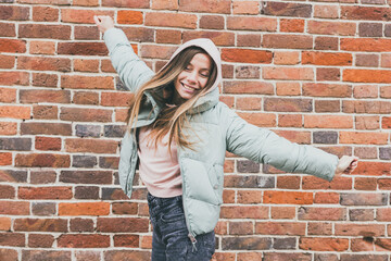 Joyful woman in pastel jacket raising arms and smiling outdoors. Urban freedom, positive energy, and expression of happiness in city life.