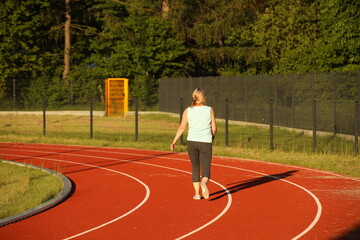 Fototapeta premium A woman runs on the treadmill of a stadium around a football field. Artificial cover of the sports complex. Activity for weight loss and a healthy lifestyle. Preparing for the competition. Free time