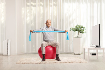 Elderly man sitting on a ball and exercising with a resistance band