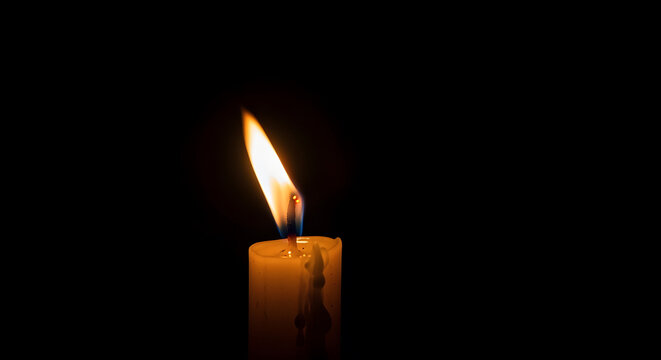 A single candle burning in the dark, its flame flickering gently in a soft breeze. Black background, central focus on light and shadow