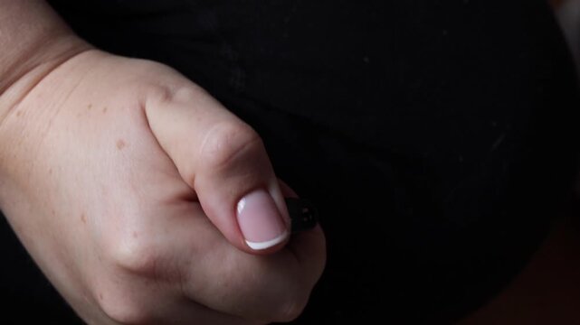 Close-up of a hand igniting a small gas lighter by pressing the ignition button with a thumb, creating a visible flame in a dark background