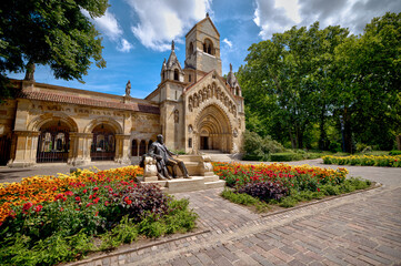 Budapest, Hungary - July 27, 2025: The Romanesque-style Jak Chapel and the Anonymous statue at Vajdahunyad Castle in City Park, surrounded by colorful summer gardens  © Torval Mork
