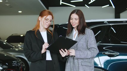 A saleswoman engages with a client in an automobile dealership, discussing car options and preparing for a test drive while reviewing paperwork and financing details.