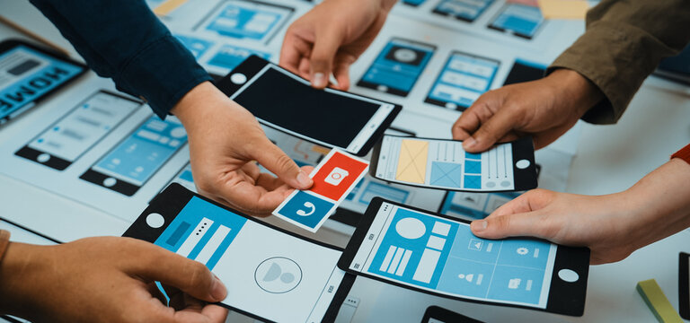 A diverse group of individuals actively collaborates on smartphone app wireframe designs during a creative workshop, showcasing teamwork and innovation in digital prototyping. SACTR - Powered by Adobe