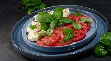 Classic Caprese salad with sliced ​​fresh tomatoes, mozzarella and basil leaves on a blue plate