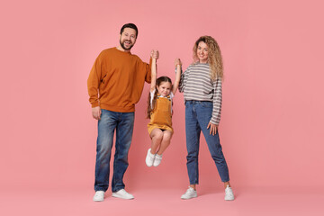 Happy parents and their daughter having fun on pink background. Family bonding
