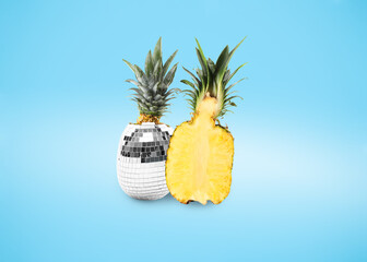 Disco ball fruit with green leaves and half of pineapple on light blue gradient background