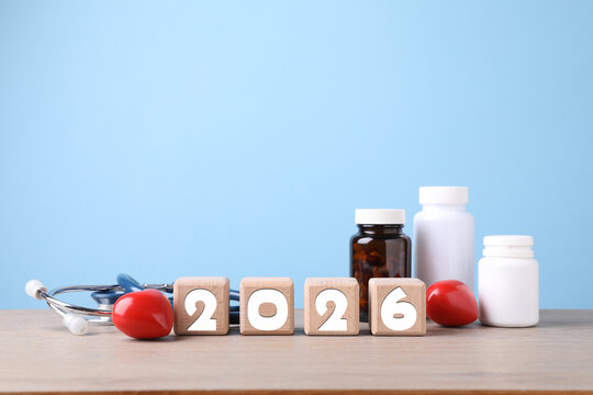 New 2026 year. Cubes with numbers, hearts, pills and stethoscope on table against light blue background