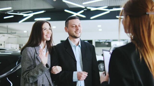 A saleswoman engages with a couple at an automobile dealership, discussing credit options and finalizing their car purchase with a handshake and paperwork.