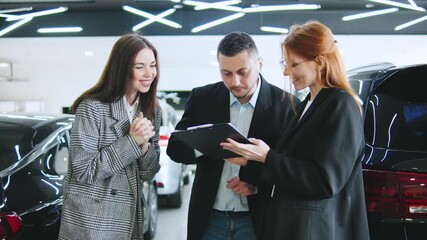 Consultation with family couple at an automobile dealership where a saleswoman discusses the contract with a buyer interested in a test drive and a potential purchase