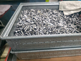 Galvanized container overflowing with machined metal pins and a towel, possibly used in a manufacturing environment