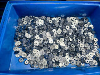 A blue container filled with metallic washers awaiting their purpose