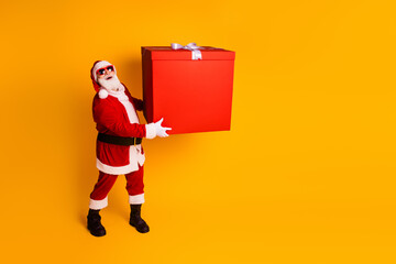 Santa in bright red suit with a large gift box on a vibrant yellow backdrop delivering holiday gift exchange and Christmas cheer