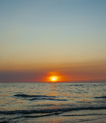 Obraz premium serene vertical image capture beauty sunset over calm ocean. sun low on horizon casting warm golden glow across sky and reflect off gentle wave. warm orange near creating peaceful calm atmosphere.