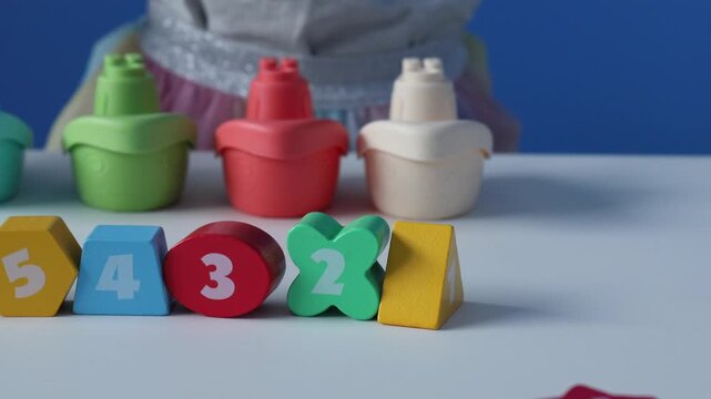 colorful wooden number blocks arranged in a row from five to one, early learning toys with geometric shapes and numerals, plastic toy bottles behind, promoting toddler learning through play