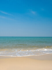Peaceful vertical tropical sea beach with gentle waves rolling onto golden sand under bright blue sky with fluffy white clouds. relaxing summer scene perfect scene for travel holliday and nature lover