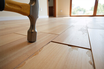 Close-up of a hammer smashing a water-damaged hardwood floor, representing DIY home improvement, demolition, or insurance claims. Concept of construction, renovation, and repair work