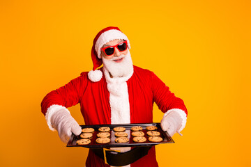 Santa in a red suit with white beard and festive hat presents a tray of cookies against a bold...