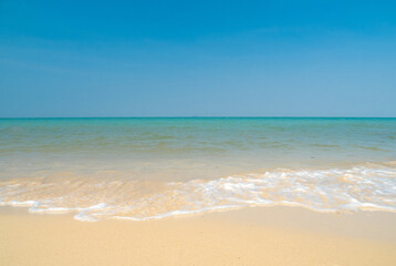 Fototapeta premium Peaceful panorama tropical sea beach with gentle waves rolling onto golden sand under bright blue sky with fluffy white clouds. relaxing summer scene perfect scene for travel holliday and nature lover