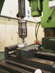 Close-up of metal drilling process using an industrial drill press machine in workshop. worker wearing protective gloves securing the workpiece in vise, demonstrating precision machining and safety