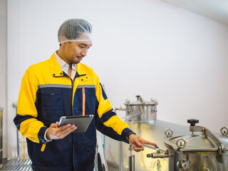 factory man worker in uniform wearing hairnet inspect stainless steel industrial equipment while use tablet. clean and organized environment reflect safety and hygiene standard in modern manufacturing