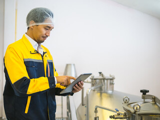 factory man worker in uniform wearing hairnet inspect stainless steel industrial equipment while use tablet. clean and organized environment reflect safety and hygiene standard in modern manufacturing