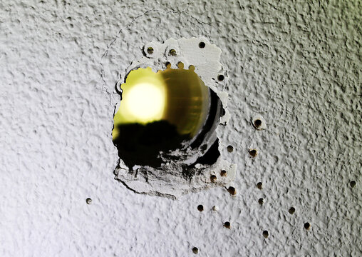 Agujero, orificio y taladros de obra y reforma en pared de gotel&eacute; blanca con luz amarilla al fondo