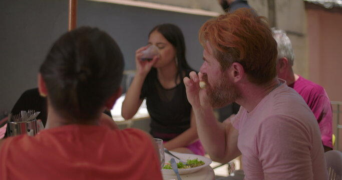 Group of friends united for lunch in a backyard BBQ setting, with a close-up of a bearded man laughing heartily, a woman in the background smiling, conveying joy and connection - Powered by Adobe
