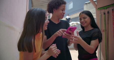 Teenagers gathered around a smartphone in suburban alleyway, sharing and enjoying social media...