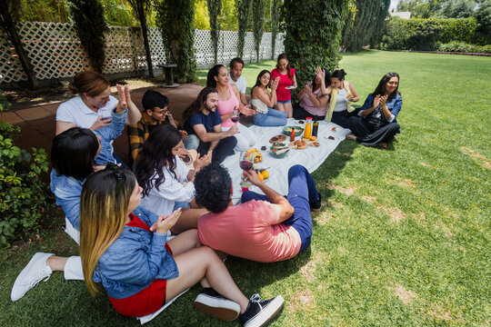 Big latin family sitting on picnic blanket in park during weekend Sunday sunny day in Mexico Latin America. Hispanic diverse and multi generation people in outdoors activities