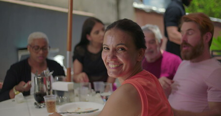 Group of friends and family seated at an outdoor table during a family BBQ lunch, sharing laughter and joyful moments in a warm and casual gathering