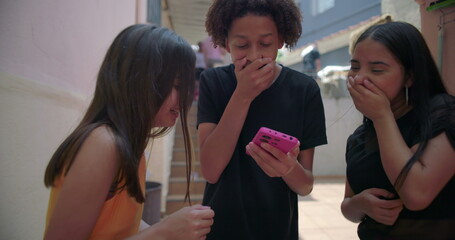 Teenagers laughing and reacting to funny video on smartphone in suburban alleyway, cheerful and...
