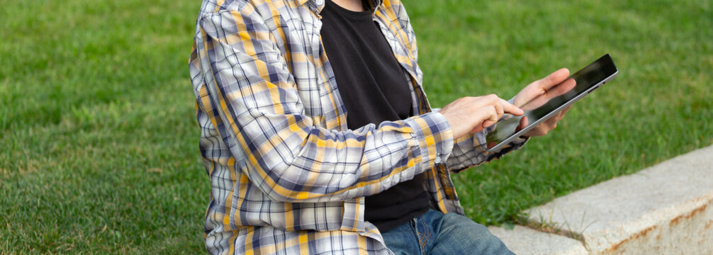 Man sitting on grass using tablet for work or study in sunny outdoor environment. Digital freedom, remote work, and mobile lifestyle.