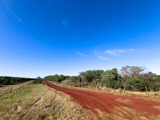 Red Dirt Road Through Countryside Under Clear Blue Sky