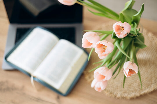 A bouquet of tulips in a vase, an open Bible and a laptop on a wooden table.
