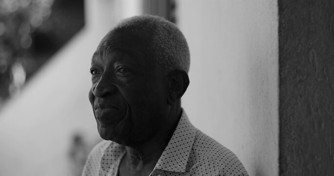 Elderly man looking sideways with a contemplative expression, leaning casually against a wall in an outdoor setting, exuding wisdom and introspection, black and white