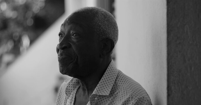 Elderly man looking sideways with a contemplative expression, leaning casually against a wall in an outdoor setting, exuding wisdom and introspection, black and white