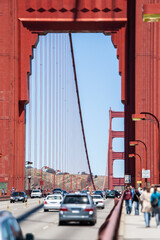 Fototapeta premium Golden Gate bridge carrying vehicle traffic and pedestrians walking on the pedestrian path, framed by the iconic red structures under a clear blue sky