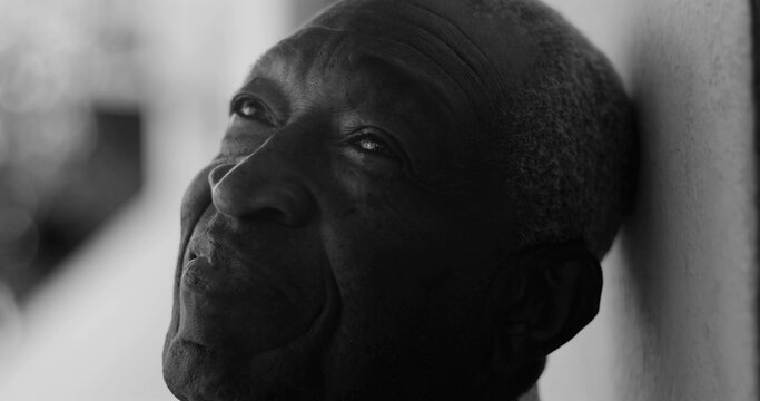 African American elderly man gazing upward with a serene expression, leaning against a wall in black and white, exuding calmness, wisdom, and introspection