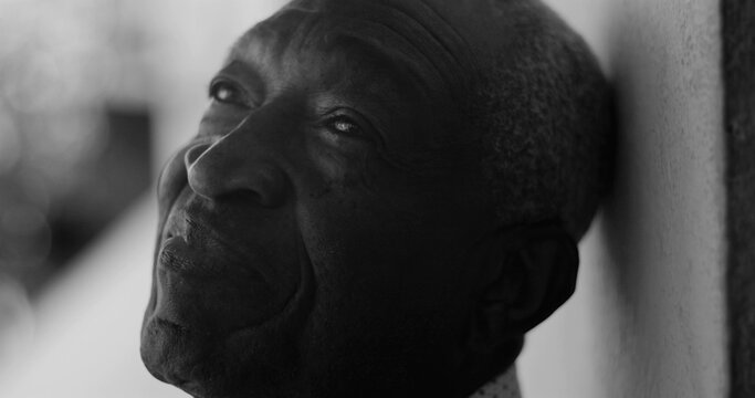 African American elderly man gazing upward with a serene expression, leaning against a wall in black and white, exuding calmness, wisdom, and introspection - Powered by Adobe