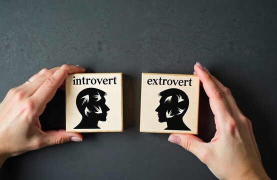 Two hands hold wooden blocks representing introvert, extrovert personalities. One block shows profile silhouette with arrows indicating inward focus, labeled introvert. Block displays similar