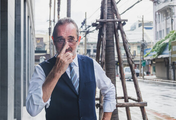 business man senior in formal suit stand confidently with ooking ahead on city street. Modern building, palm trees, and urban element in background create professional and metropolitan atmosphere.