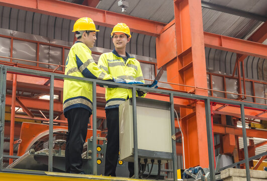 Leader manager talk work order staff engineer technician team in hard hat and uniform safety vest hand holding laptop discuss inspection check heavy machine technology product in industry factory