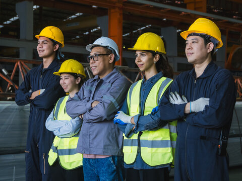group five industrial worker standing together in factory setting, wearing safety helmets and reflective vest. image represent teamwork, safety compliance, professionalism in industrial environment.