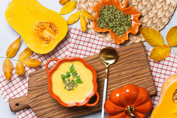 Bowl of pumpkin soup with seeds and herbs on woven placemat.