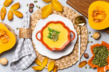 Bowl of pumpkin soup with seeds and herbs on woven placemat.
