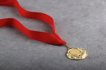 Gold medal with red ribbon on grey background. Reward for victory.
