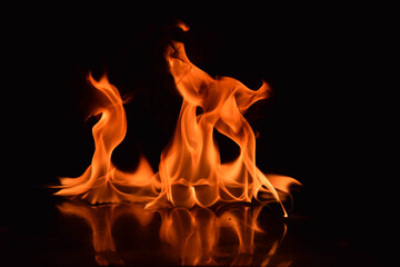 A captivating image of two orange flames rising and twisting in unison, mirrored on a shiny surface with a black background, highlighting the dynamic energy and graceful forms of fire in motion.

