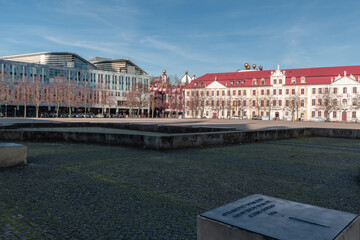 Modern glass facades of the DomQuartier meet the colorful Green Citadel with its golden domes on Magdeburg’s Domplatz under a clear blue sky. © Heidi