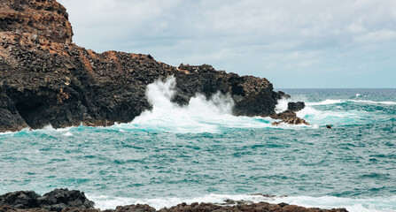 Background: volcanic coastal cliff with waves on a cloudy day.